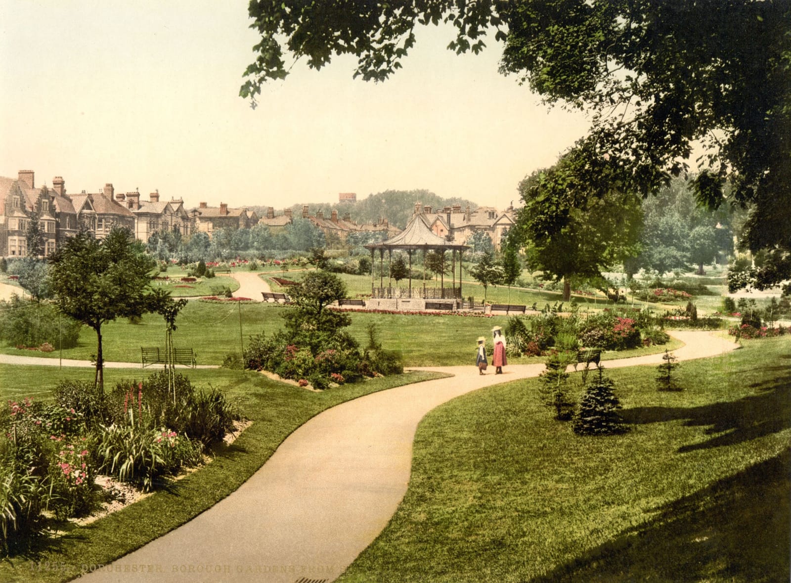A curving path through lawns and flower beds to a bandstand, with trees and houses around.