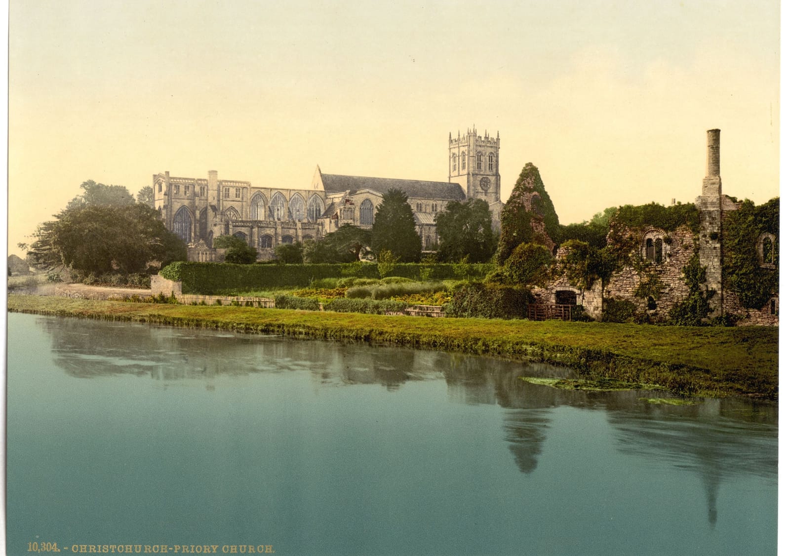The long priory church and its tower reflected in the still river in front of it.