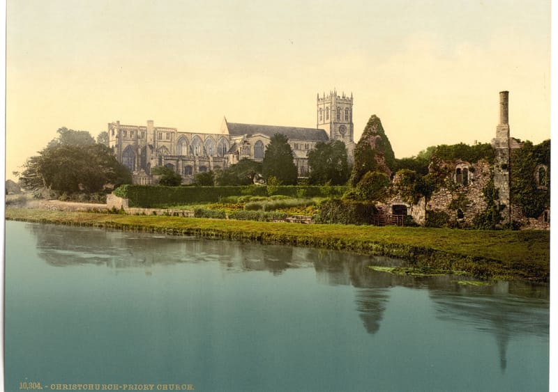 The long priory church and its tower reflected in the still river in front of it.