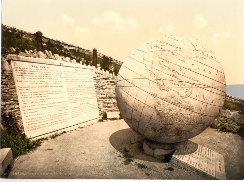 A huge stone globe of the world on a terrace, with carved stone tablets set in the wall behind it.