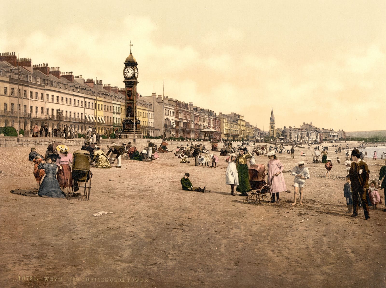 Families on the sands in front of the clock tower, with the long terrace of the seafront behind.