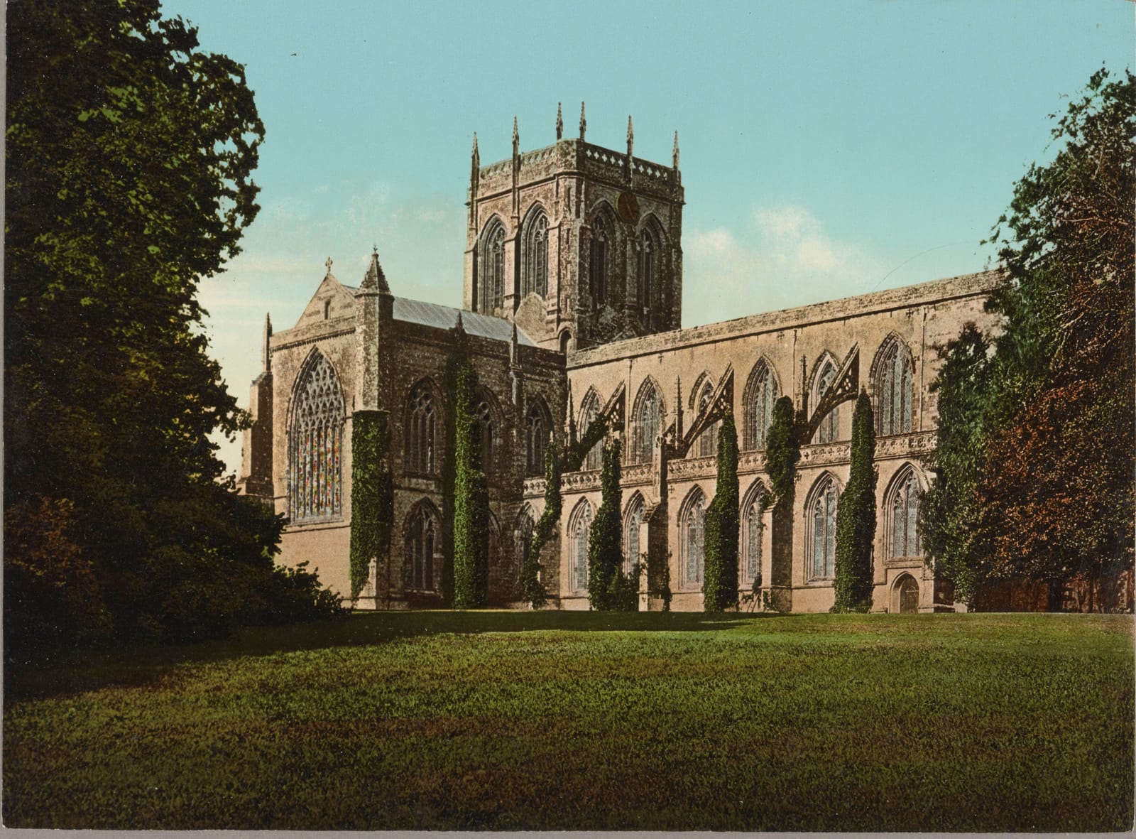 The tall abbey church at Milton Abbas on a bright lawn, framed by dark trees under a blue sky.