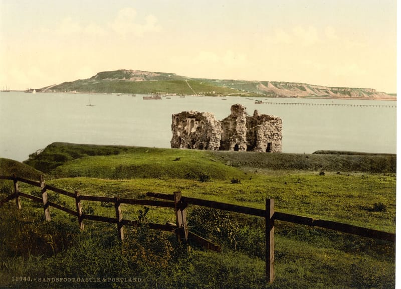 The ruin of a small stone castle on a grassy clifftop, looking across the water to Portland.