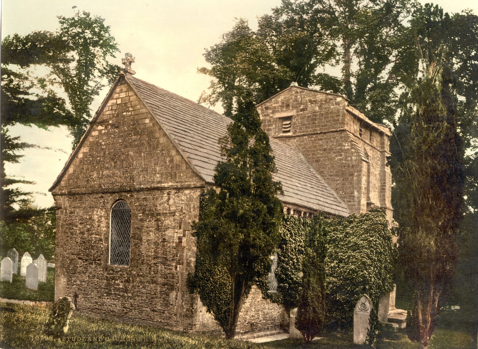 A small squat Norman stone church among trees and yew in a quiet churchyard.