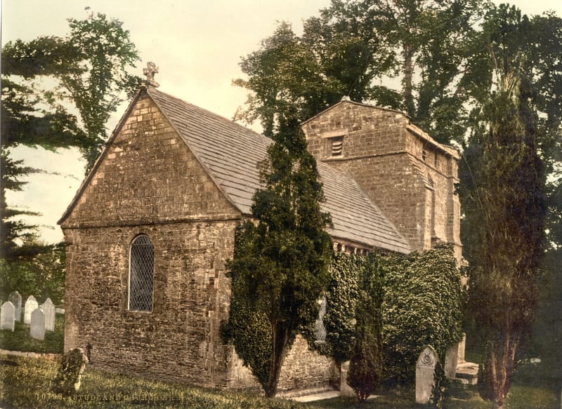 A small squat Norman stone church among trees and yew in a quiet churchyard.