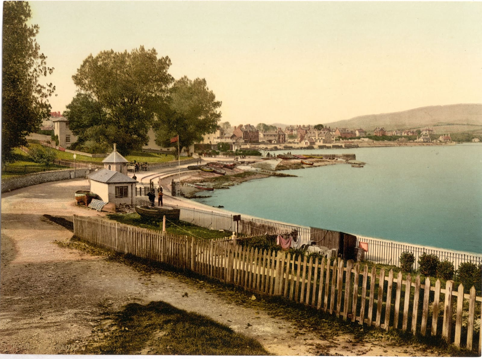 A path along a wooden fence above the bay at Swanage, with the town and hills across the water.