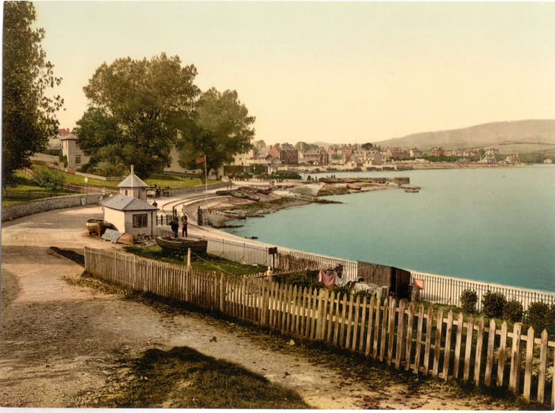 A path along a wooden fence above the bay at Swanage, with the town and hills across the water.